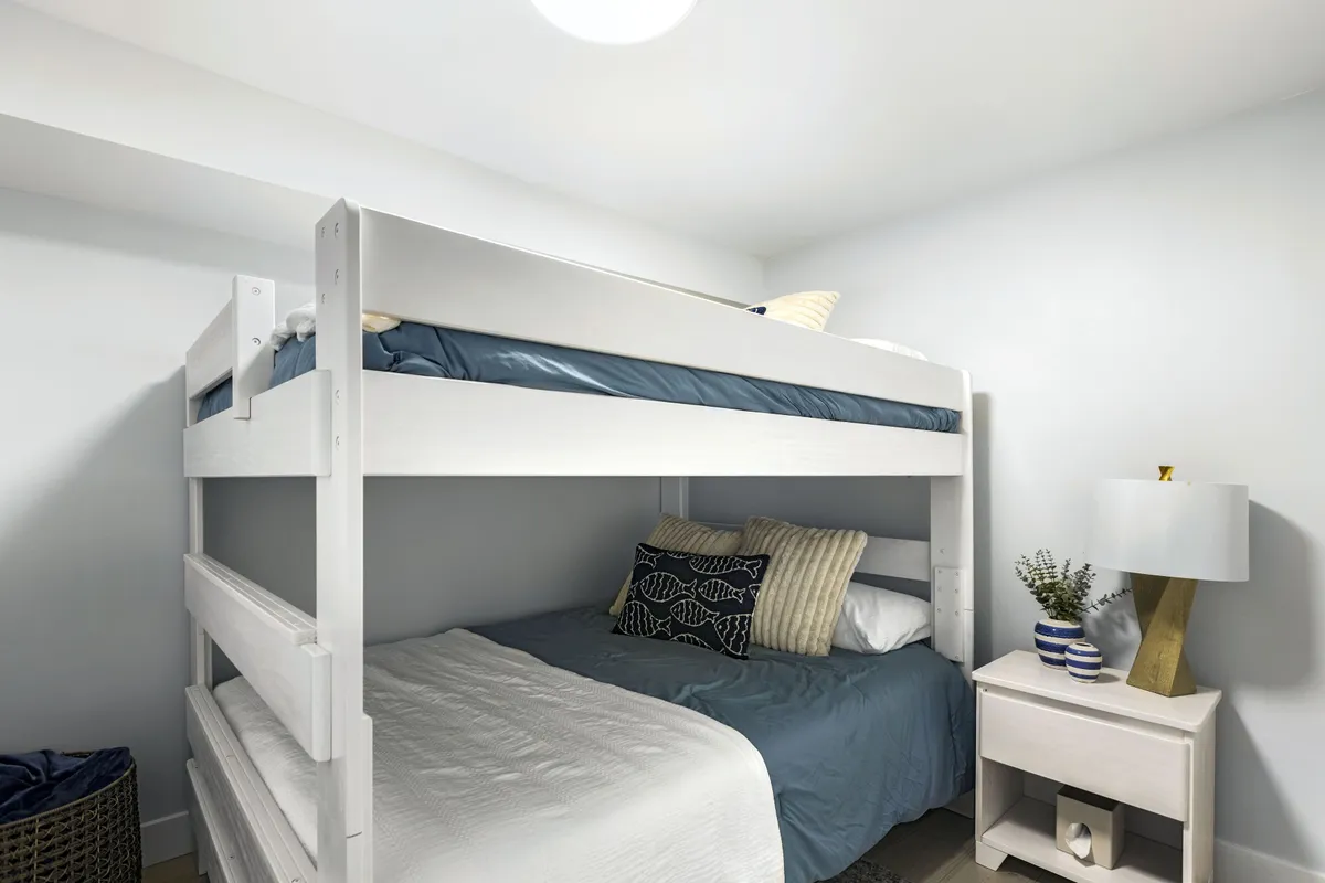 A well-lit room featuring a comfortable bunk bed dressed in decorative pillows, with a nightstand beside for convenience. The overall mood is cozy and welcoming, making it suitable for children or additional guests in a flexible family setup.