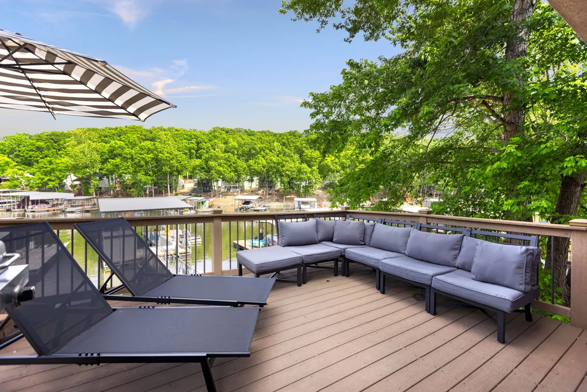 This image highlights a beautiful outdoor seating area overlooking the lake, complete with comfortable chairs and a shade umbrella. The inviting scene suggests a space perfect for groups to gather, enjoy drinks or meals, and soak in lakeside views from the deck.