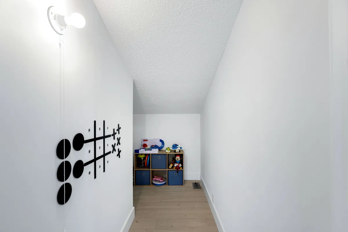 A cheerful children's play area with tic-tac-toe wall art, a toy storage unit, and bright lighting, designed specifically for family fun and creative play. The space is colorful and safe, inviting younger guests to explore and enjoy themselves.