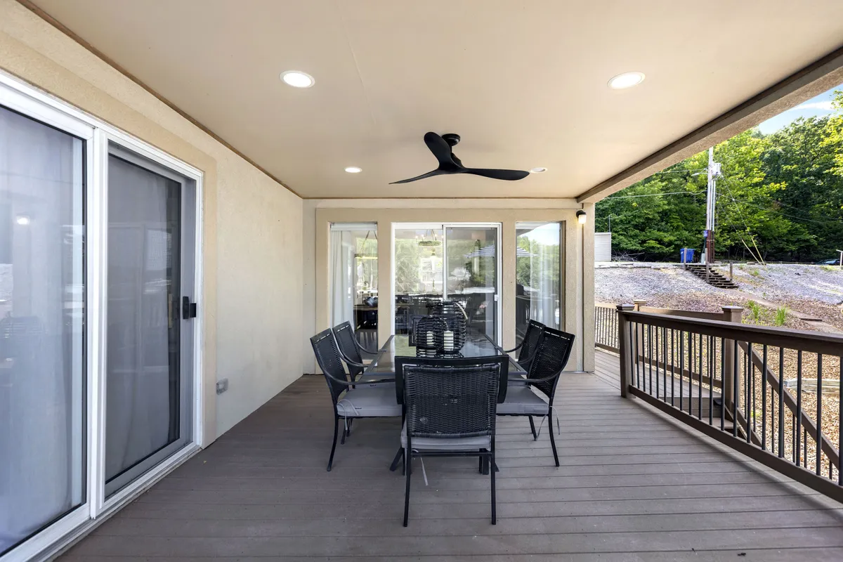 A spacious deck features a large outdoor dining table, ceiling fan, and views overlooking the water. The inviting setup is ideal for group meals and gatherings, connecting dining with the lakeside atmosphere.
