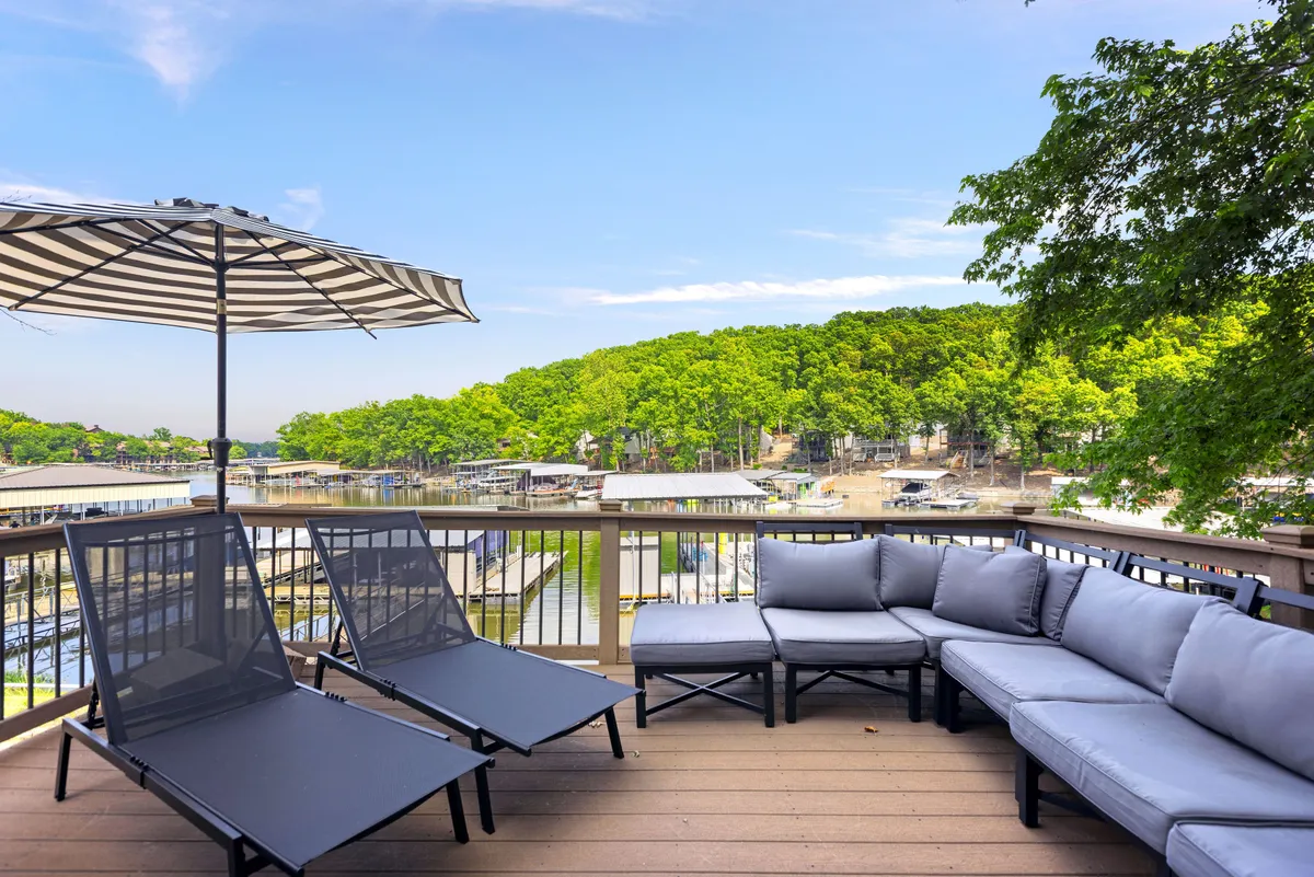 The photo features an outdoor seating area with an umbrella, surrounded by lush greenery and offering tranquil views of the lake. The setup is designed for socializing, relaxation, and enjoying the peaceful lakeside atmosphere.