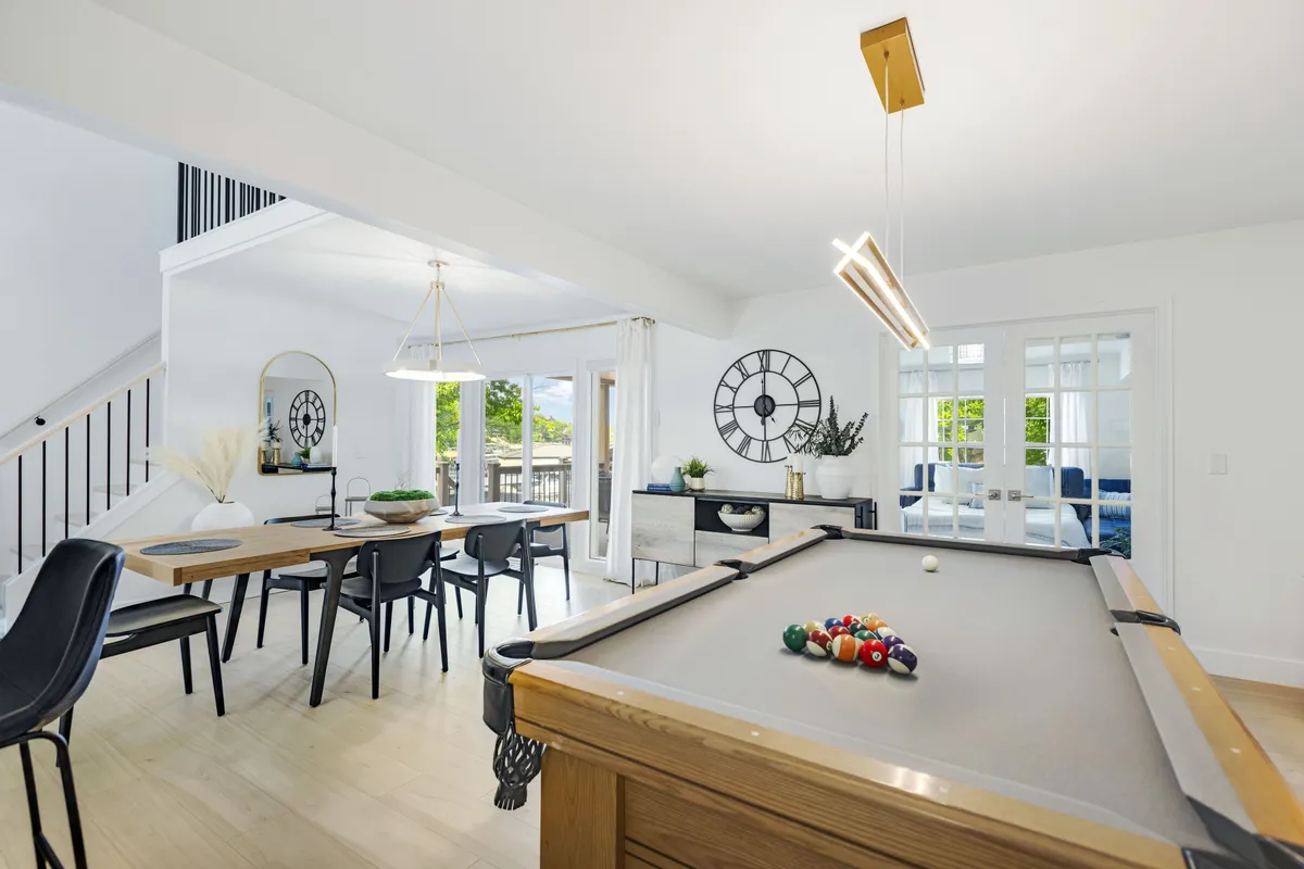 A bright, open space featuring a pool table and dining table, complemented by stylish light fixtures and large windows with natural light. The layout encourages social interaction, from friendly games to shared meals, all within a playful, welcoming atmosphere.