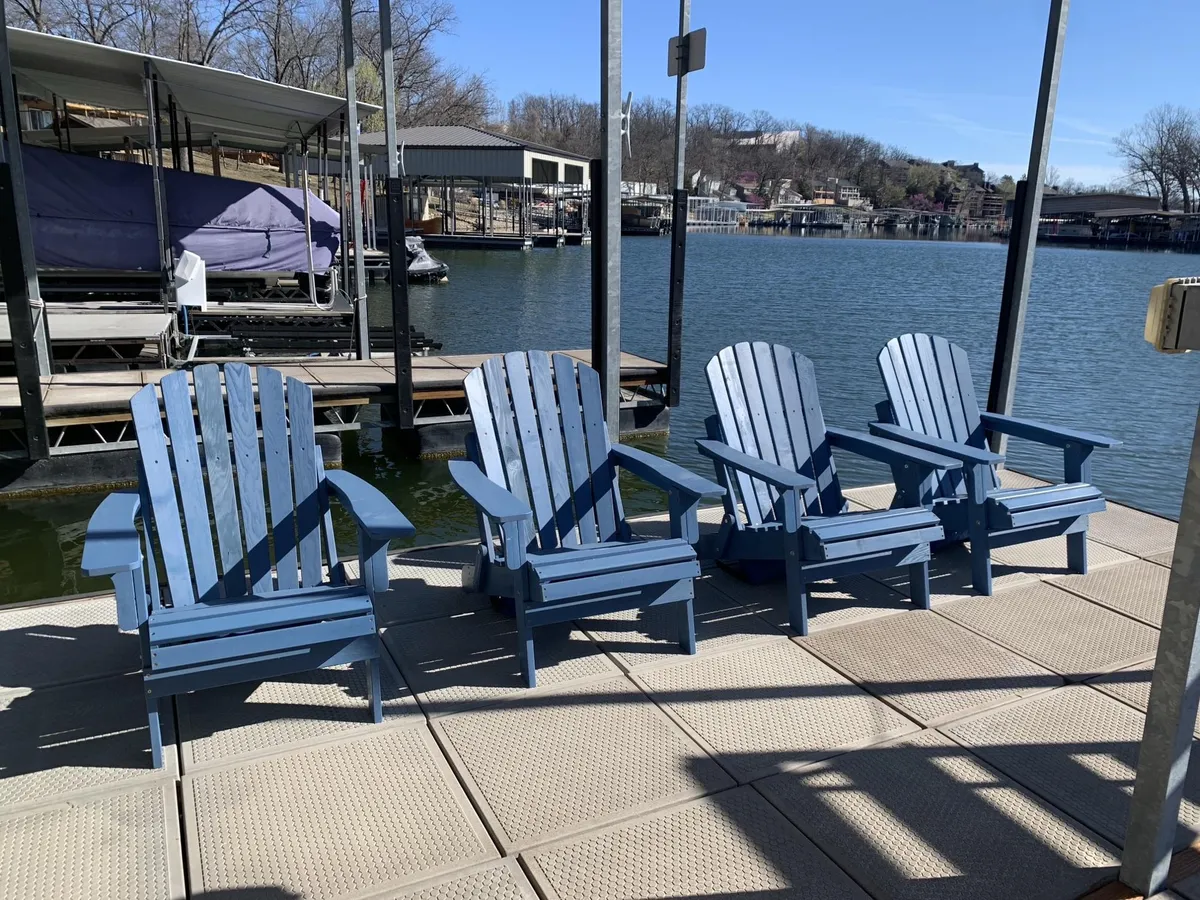This image showcases a tranquil lakeside scene with classic Adirondack chairs positioned on a wooden dock. The calm water and a boathouse are visible, framed by lush, mature trees. The scene invites relaxation and highlights the private, direct lake access central to the section's theme.