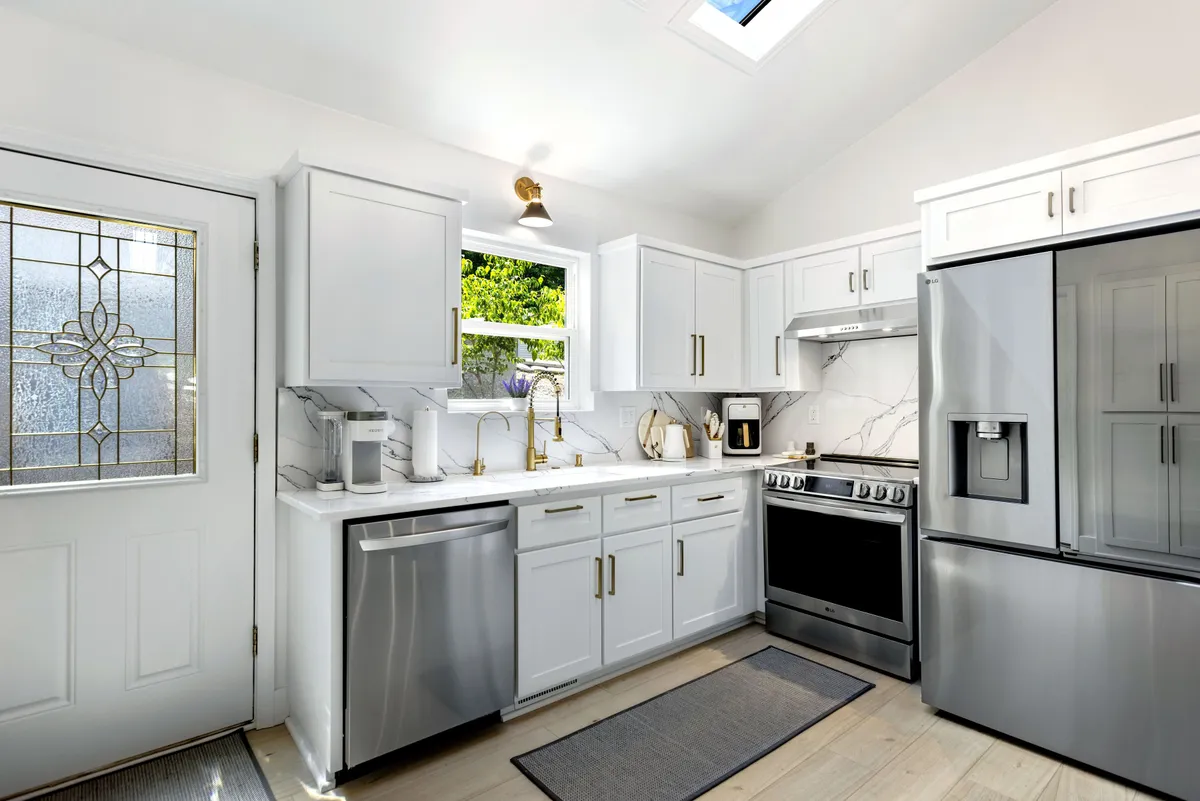 A bright, inviting kitchen featuring a central island, stainless steel appliances, a window with lush greenery outside, and a skylight that fills the room with natural light. The space is ideal for cooking, entertaining, and family gatherings.